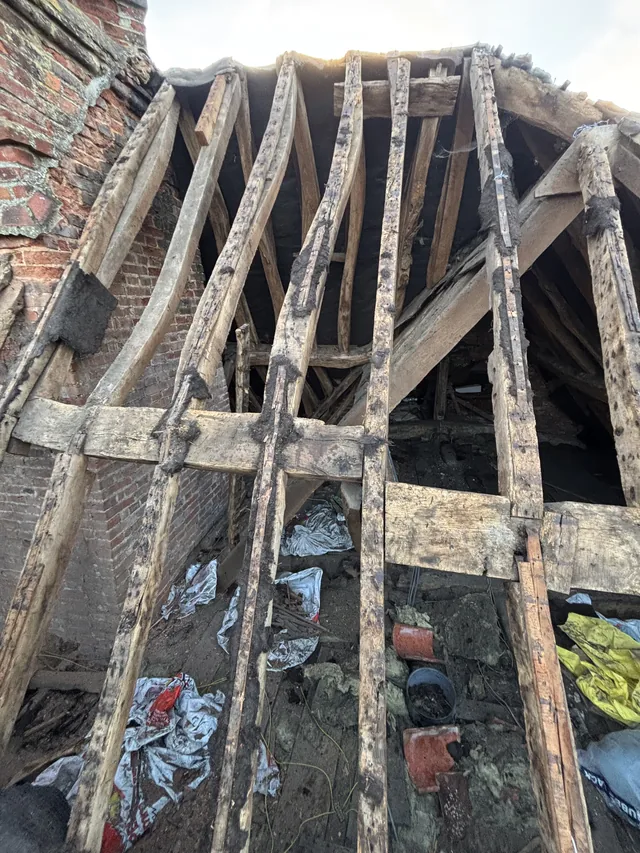 Exposed roof timbers reveal rubble and discarded materials inside an opened roof slope.
