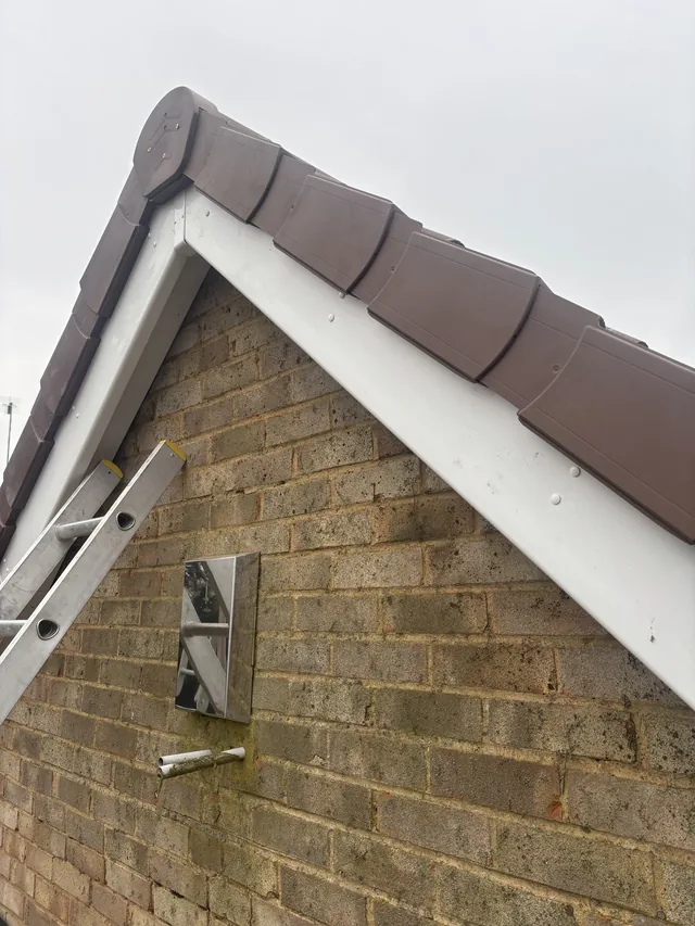 A white bargeboard follows the gable beneath brown verge caps above stone walls.