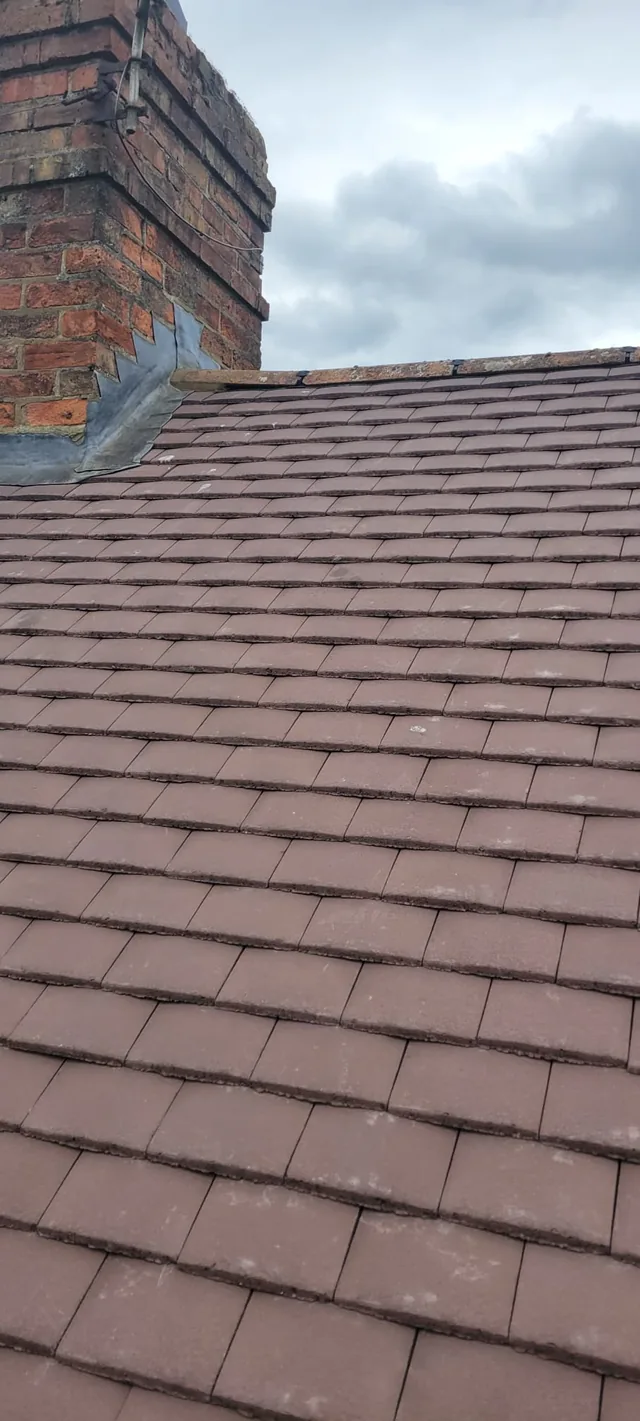 Stepped flashing meets a brick chimney above neat rows of brown roof tiles.