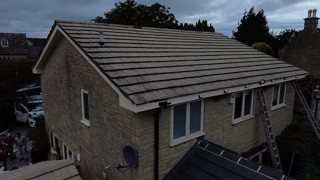 Grey tiles cover a stone house roof above white windows and ladders.