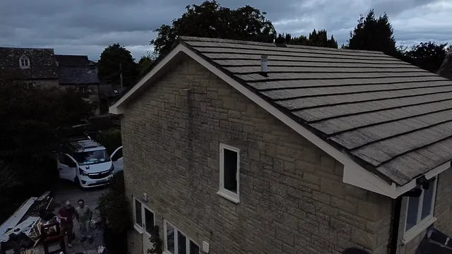 A tiled roof meets a stone gable above a driveway and parked white car.