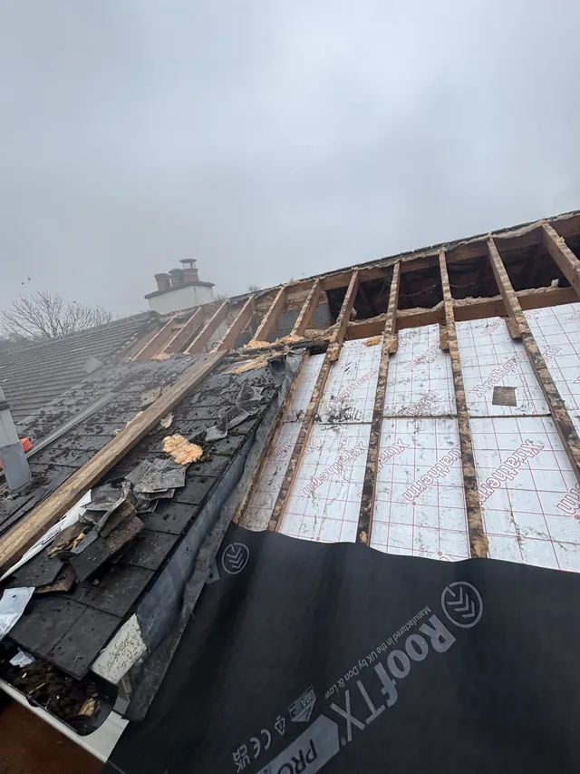 White roof panels and bare upper rafters sit beside torn roofing and dark membrane.
