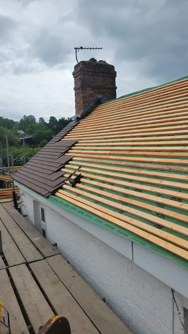 New battens and partly laid tiles sit above white fascia along a scaffolded cottage.