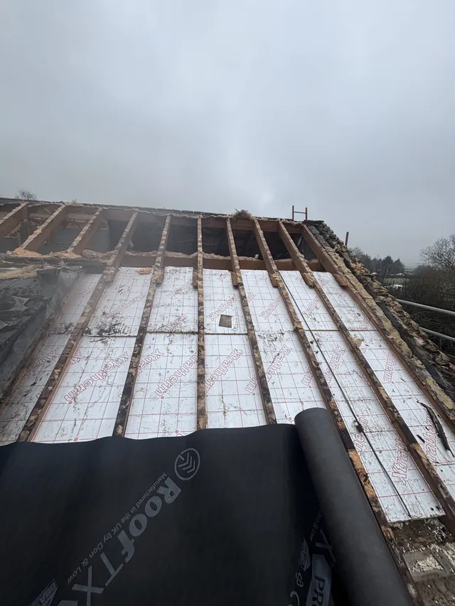 An opened roof reveals white panels between rafters above a roll of black membrane.