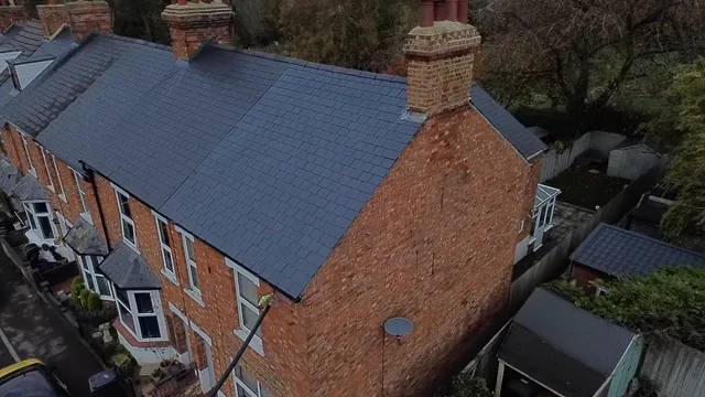 Aerial view of a grey slate roof above a red brick house and garden.