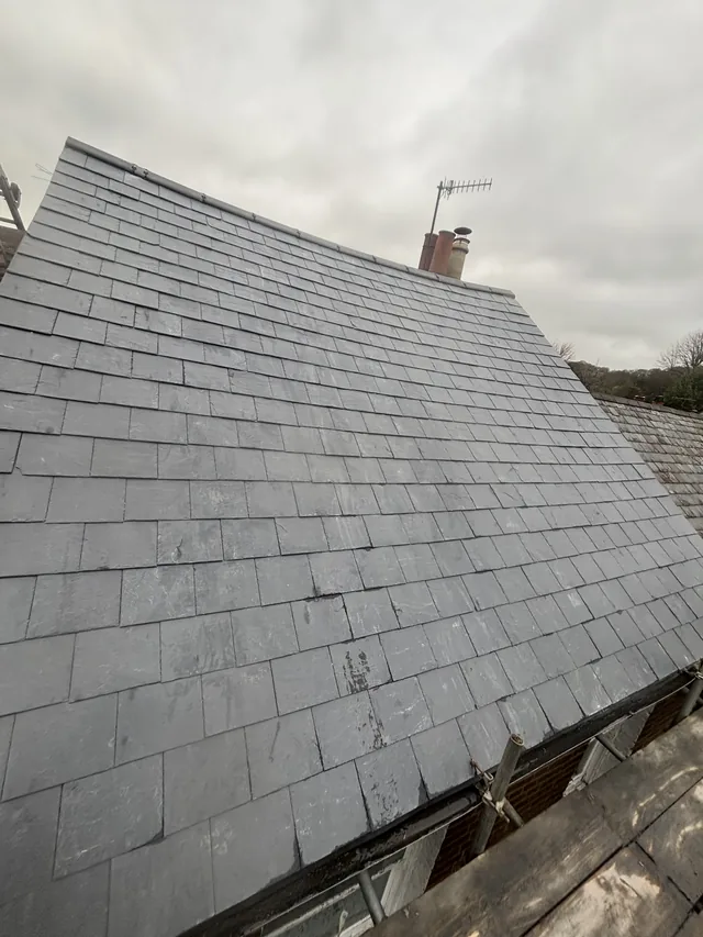 Even grey slate courses rise towards a capped ridge beneath an overcast sky.