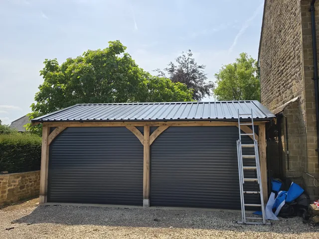 A grey profiled roof covers a timber framed double garage with matching roller doors.