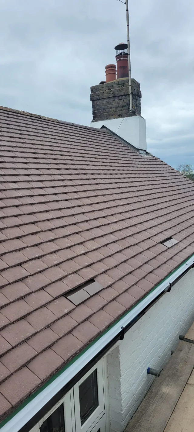 Brown roof tiles and vents rise above white fascia towards a rendered chimney.